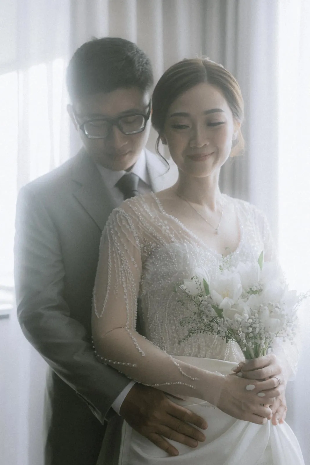 Johan memeluk Melissa dari belakang dalam cahaya jendela